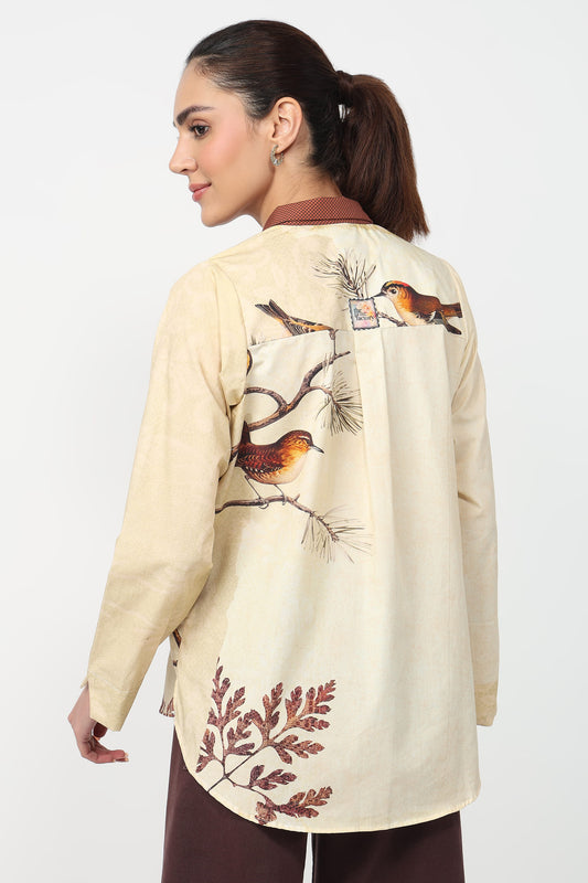 Woman wearing a beige shirt with bird and leaf designs on a white background