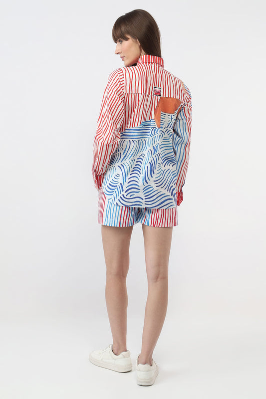 A model is shown from the back wearing a matching red, white, and blue striped shirt and shorts set with a blue and white wavy patterned back panel, paired with white sneakers on a light gray studio background.