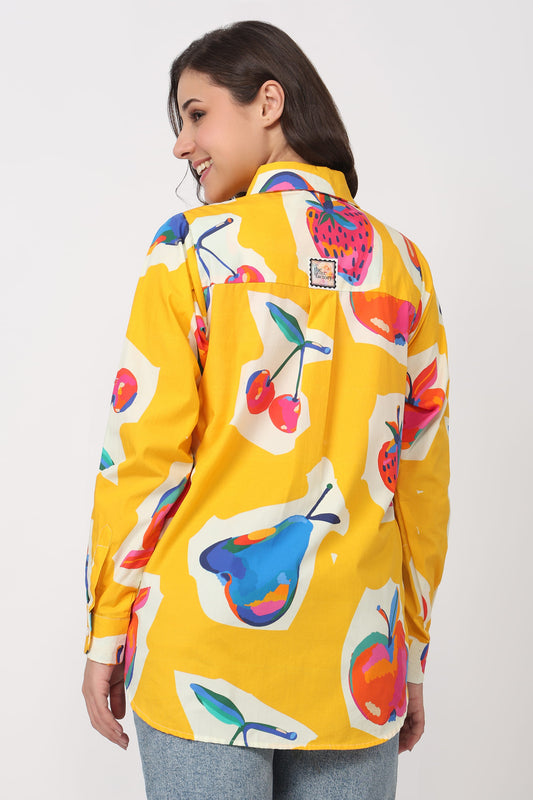 Woman wearing a yellow shirt with colourful fruit patterns on a white background