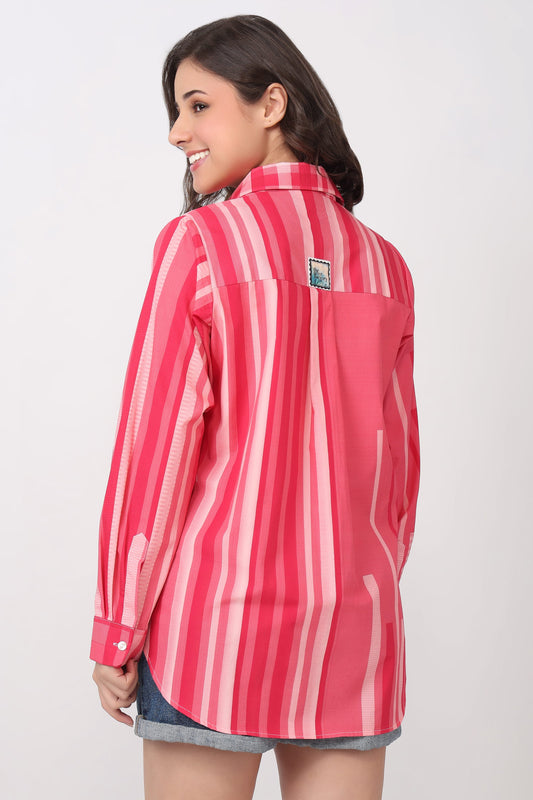 A woman shown from the back wearing a pink and white vertically striped button-up shirt with denim shorts, set against a plain light gray studio background.