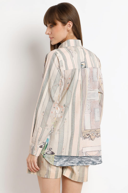 A woman shown from the back wearing a long-sleeve striped shirt and matching striped shorts. The shirt features vertical stripes in beige, cream, and muted green, with a decorative architectural print patch on the back pocket and a blue-gray patterned hem.