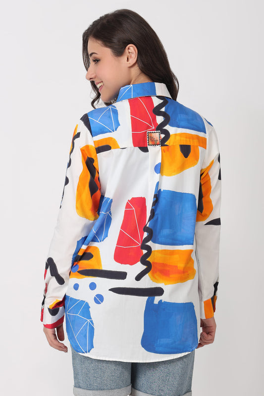 A woman shown from the back wearing a white button-up shirt with a bold abstract geometric print in blue, orange, red, and black, paired with light blue jeans against a plain light gray studio background.