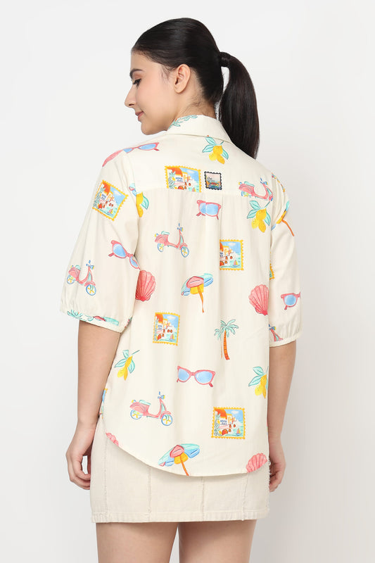 A woman shown from the back wearing a cream-colored short-sleeve button-up shirt with a colorful tropical print of palm trees, umbrellas, and scooters, paired with a matching cream mini skirt against a plain white background.