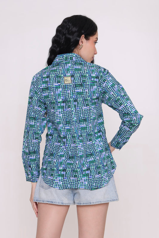 A woman shown from the back wearing a long-sleeve button-up shirt with a green, blue, and white geometric pattern, paired with denim shorts, against a plain light background.