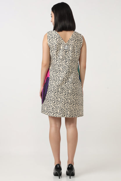 A woman viewed from the back wearing a sleeveless knee-length dress with an abstract black line pattern on a light beige background. She is holding a small colorful clutch and wearing black heels against a plain white studio background.