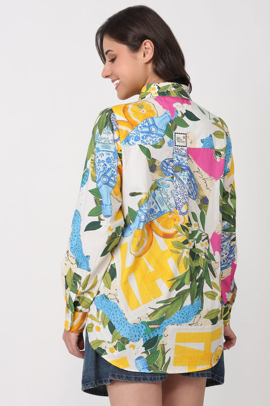 A woman shown from the back wearing a long-sleeve button-up shirt with a vibrant multicolor print featuring blue and yellow lemons, green leaves, and pink accents on a cream background.