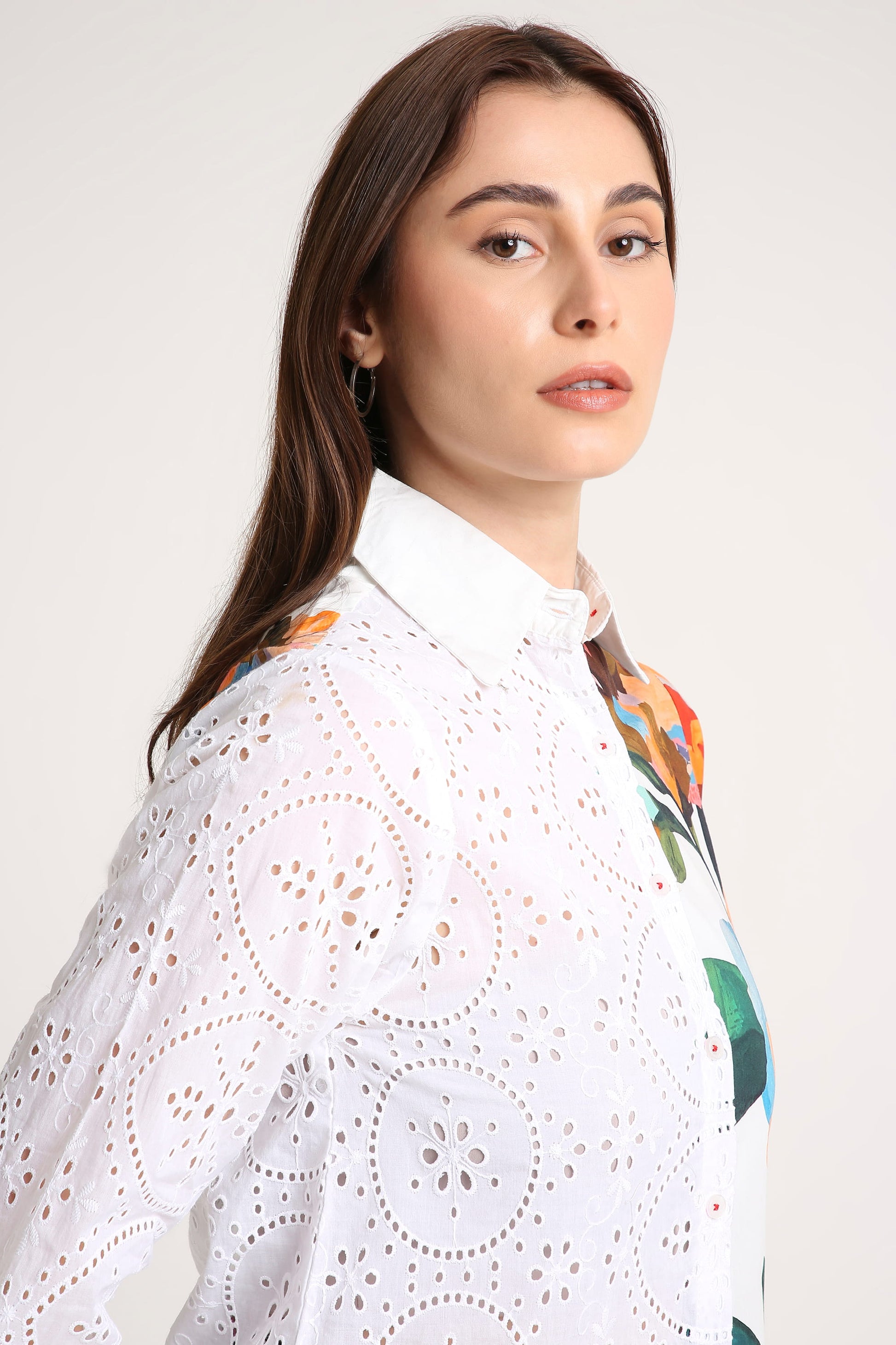 Woman wearing a white shirt with a colourful patterned shirt underneath on a plain background