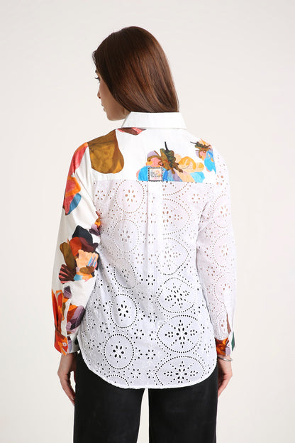 A woman shown from the back wearing a white long-sleeve button-up shirt with colorful abstract painterly prints on the shoulders and sleeves, paired with black pants, against a plain light background.