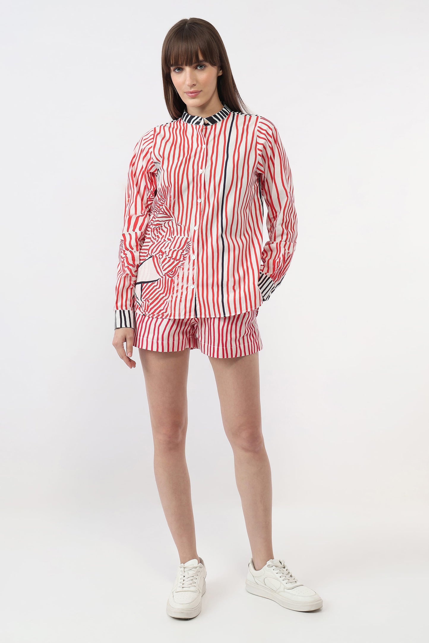 A model wearing a matching red, white, and navy striped long-sleeve button-up shirt and shorts set, paired with white sneakers, against a plain white studio background.