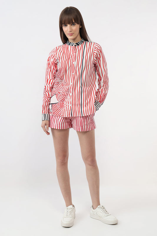 A model wearing a matching red, white, and navy striped long-sleeve button-up shirt and shorts set, paired with white sneakers, against a plain white studio background.