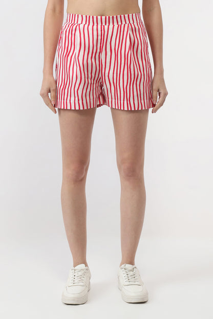 A model from the waist down wearing red and white vertically striped shorts and white sneakers, standing against a plain light gray studio background.