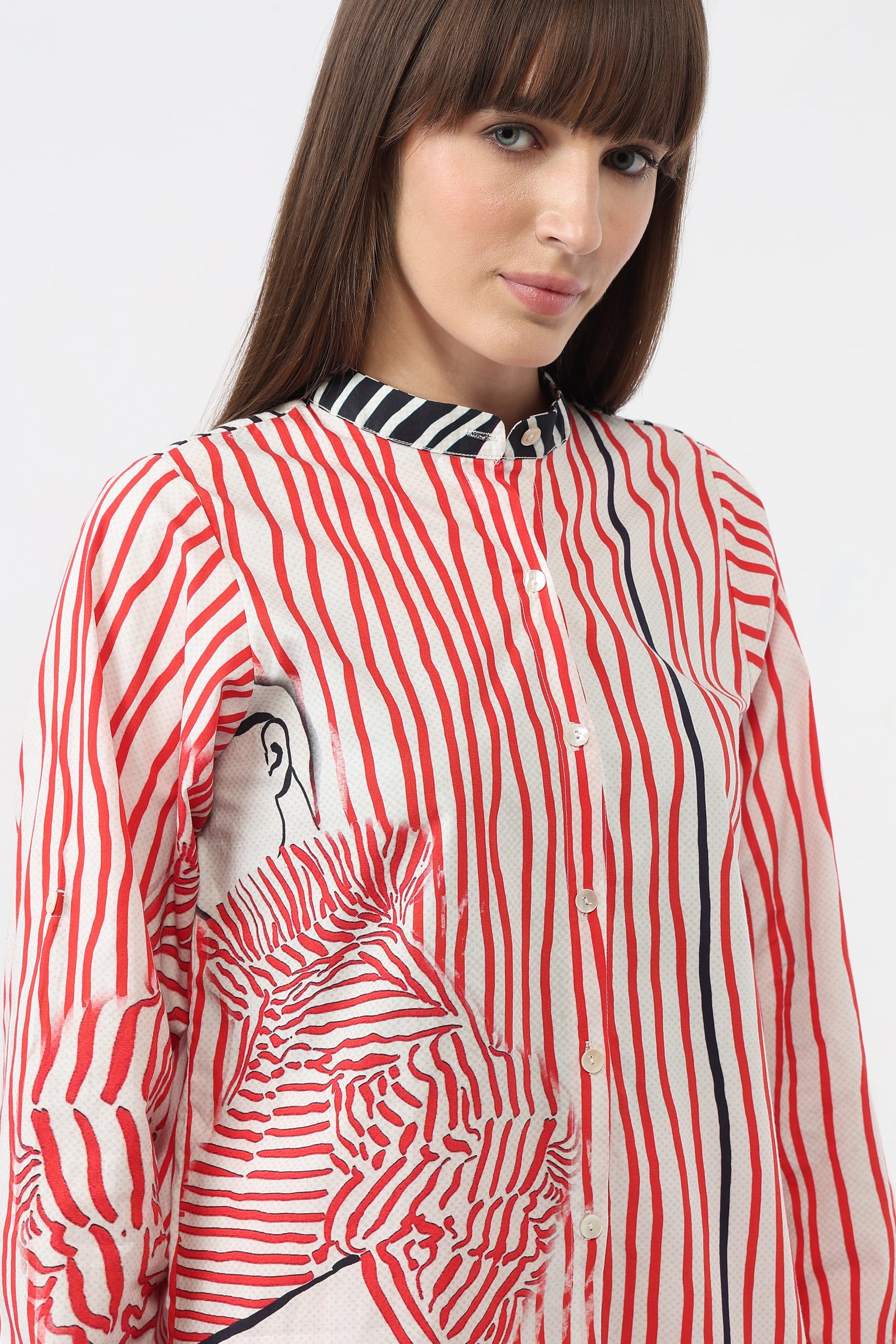 A woman wearing a long-sleeve button-up blouse with a red, white, and black vertical stripe pattern and a black-and-white striped collar, shown against a light gray studio background.