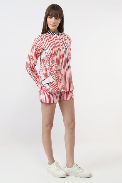 A model wearing a matching red and white striped lounge set consisting of a long-sleeve button-up shirt and shorts, paired with white sneakers, against a plain white studio background.