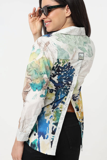 A woman shown from the back wearing a long-sleeve button-up shirt with a multicolor abstract watercolor print in blue, green, yellow, and beige on a white base, paired with black pants and sunglasses.