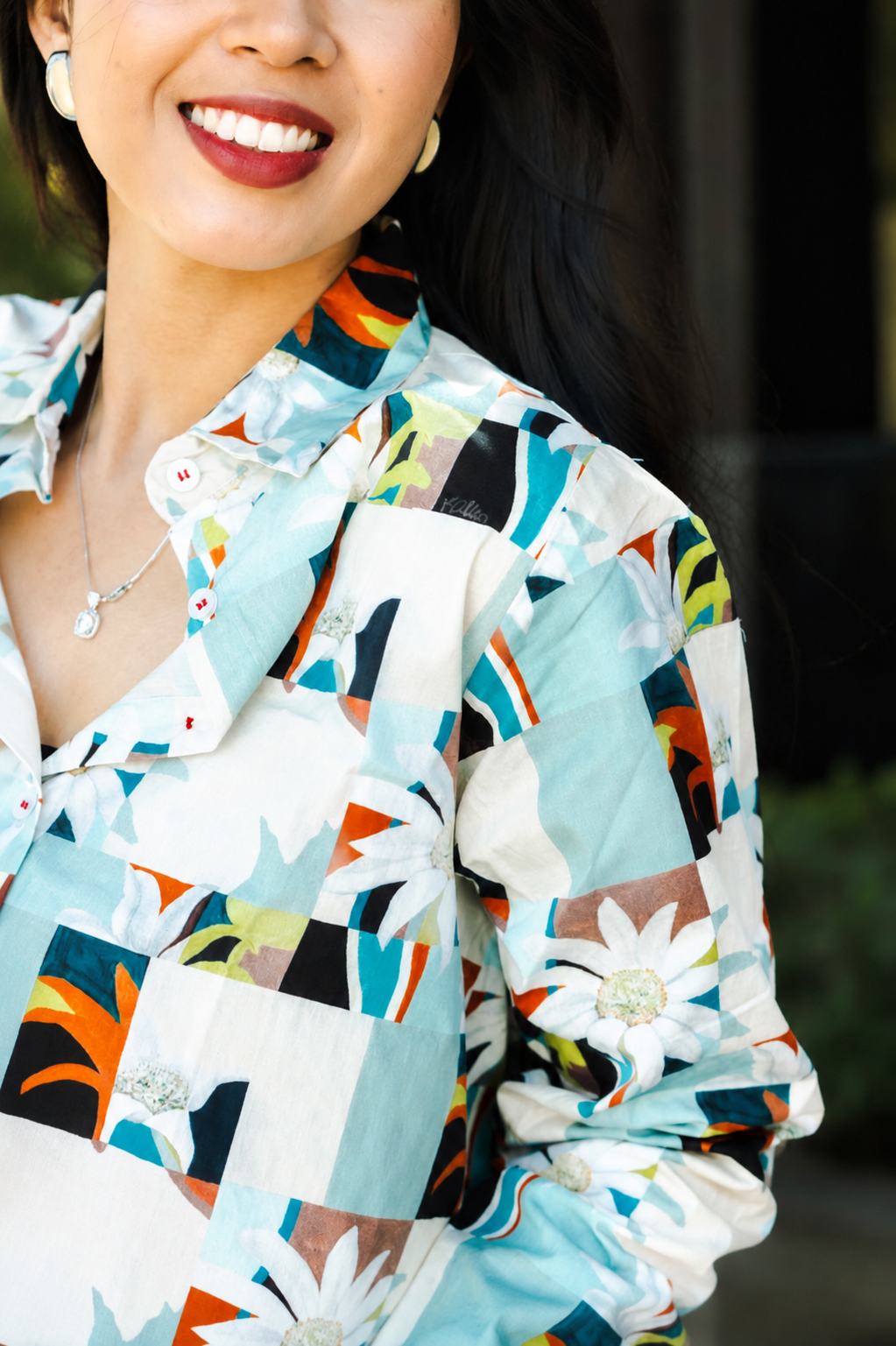 A close-up of a woman wearing a long-sleeve button-up shirt with a colorful geometric patchwork pattern in light blue, white, orange, black, and green.