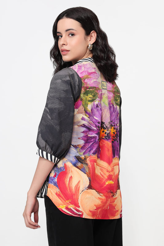 Woman wearing a colourful floral print shirt with a grey sleeve on a white background