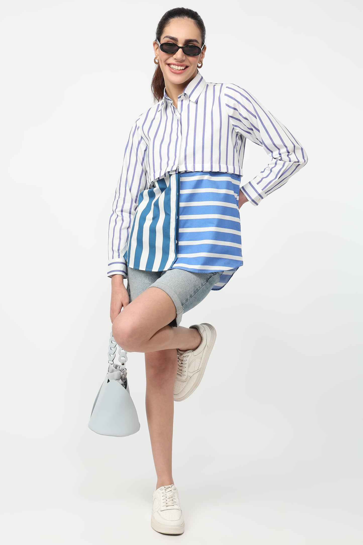 Woman wearing a striped shirt and shorts with a blue and white bag on a white background