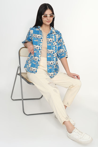 Person wearing a blue floral shirt and white pants sitting on a chair against a white background