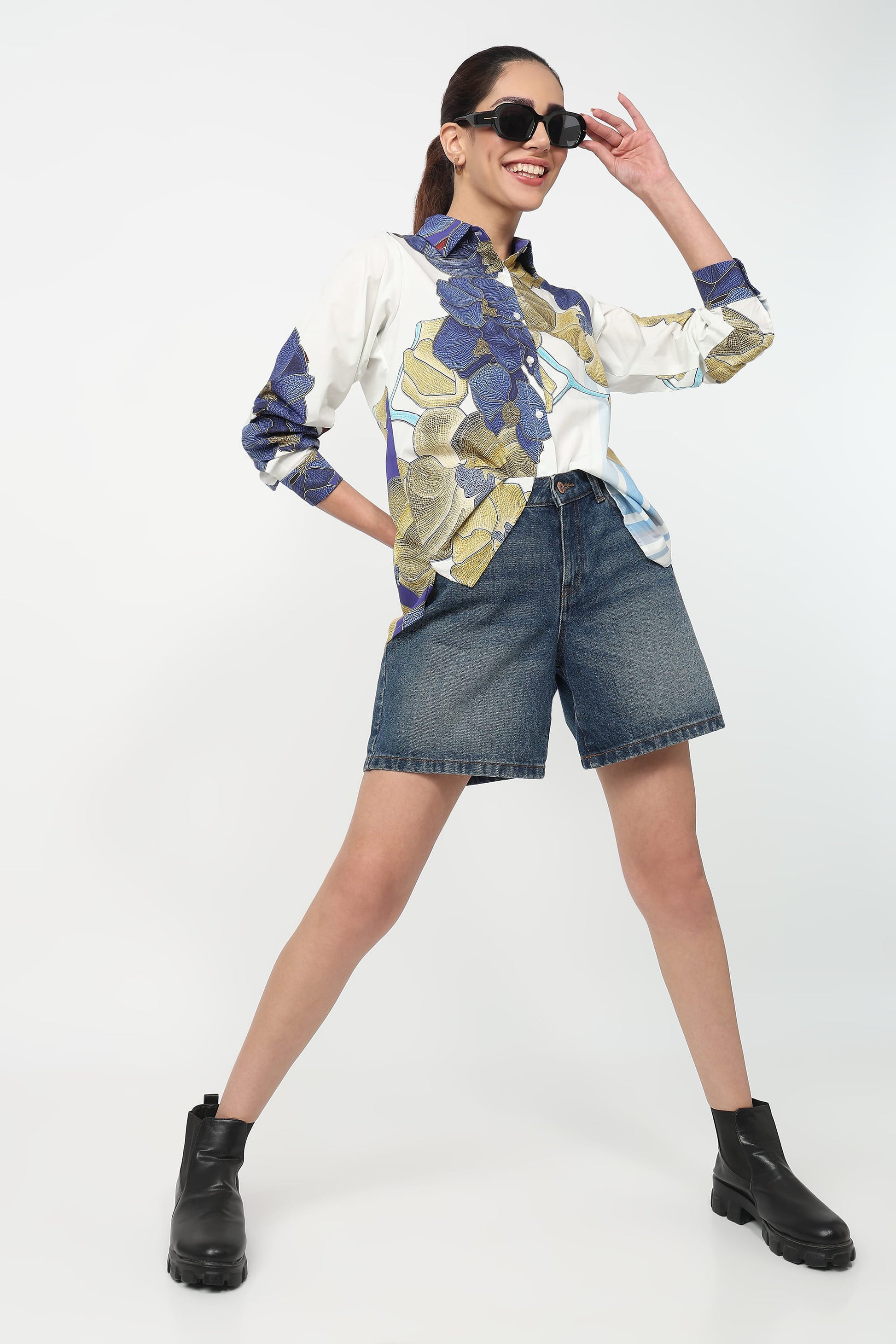 Woman wearing a patterned shirt, denim shorts, and black boots on a white background