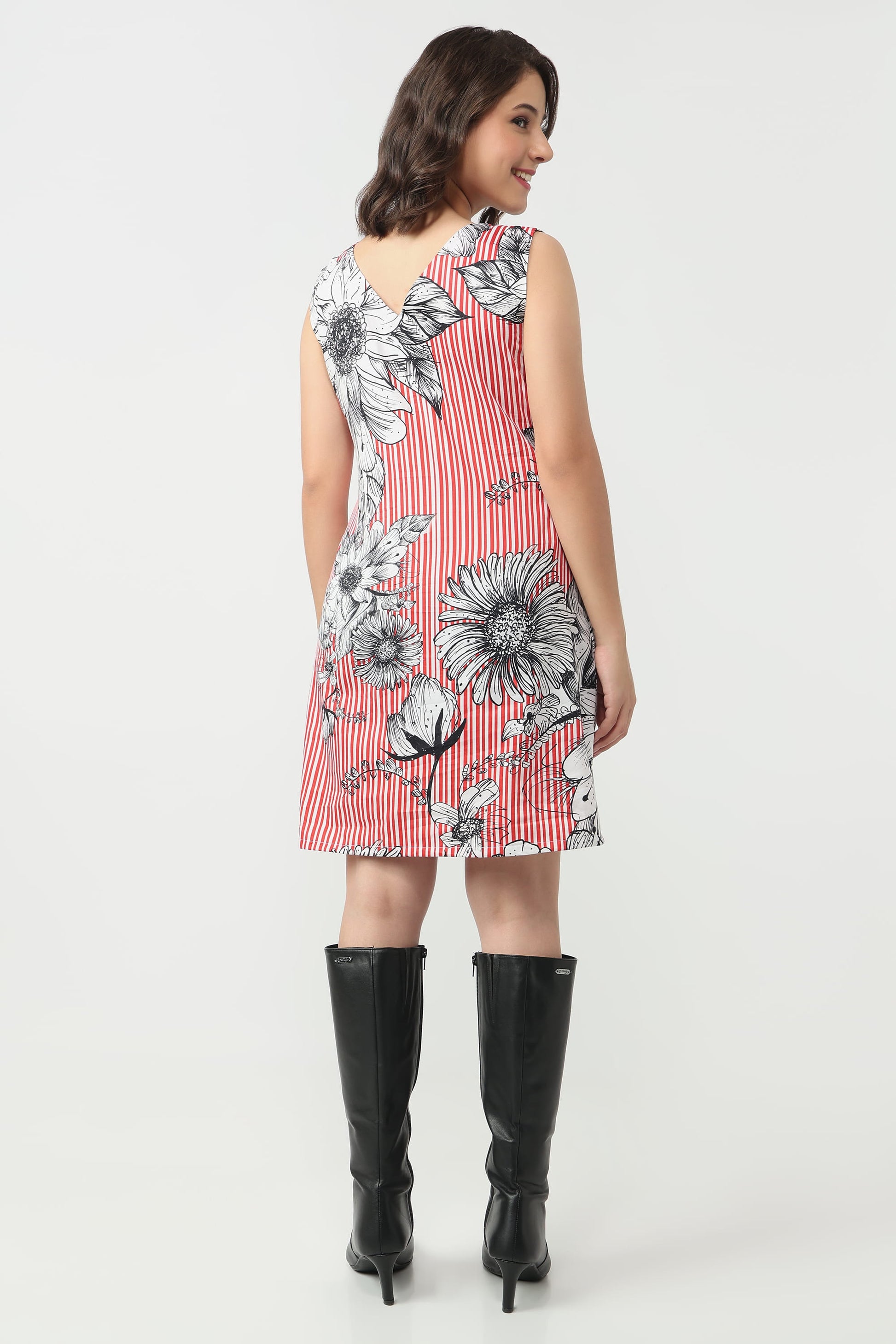 A woman shown from the back wearing a sleeveless A-line dress with a red and white striped base, black and white floral print, and black knee-high boots, against a light gray studio background.