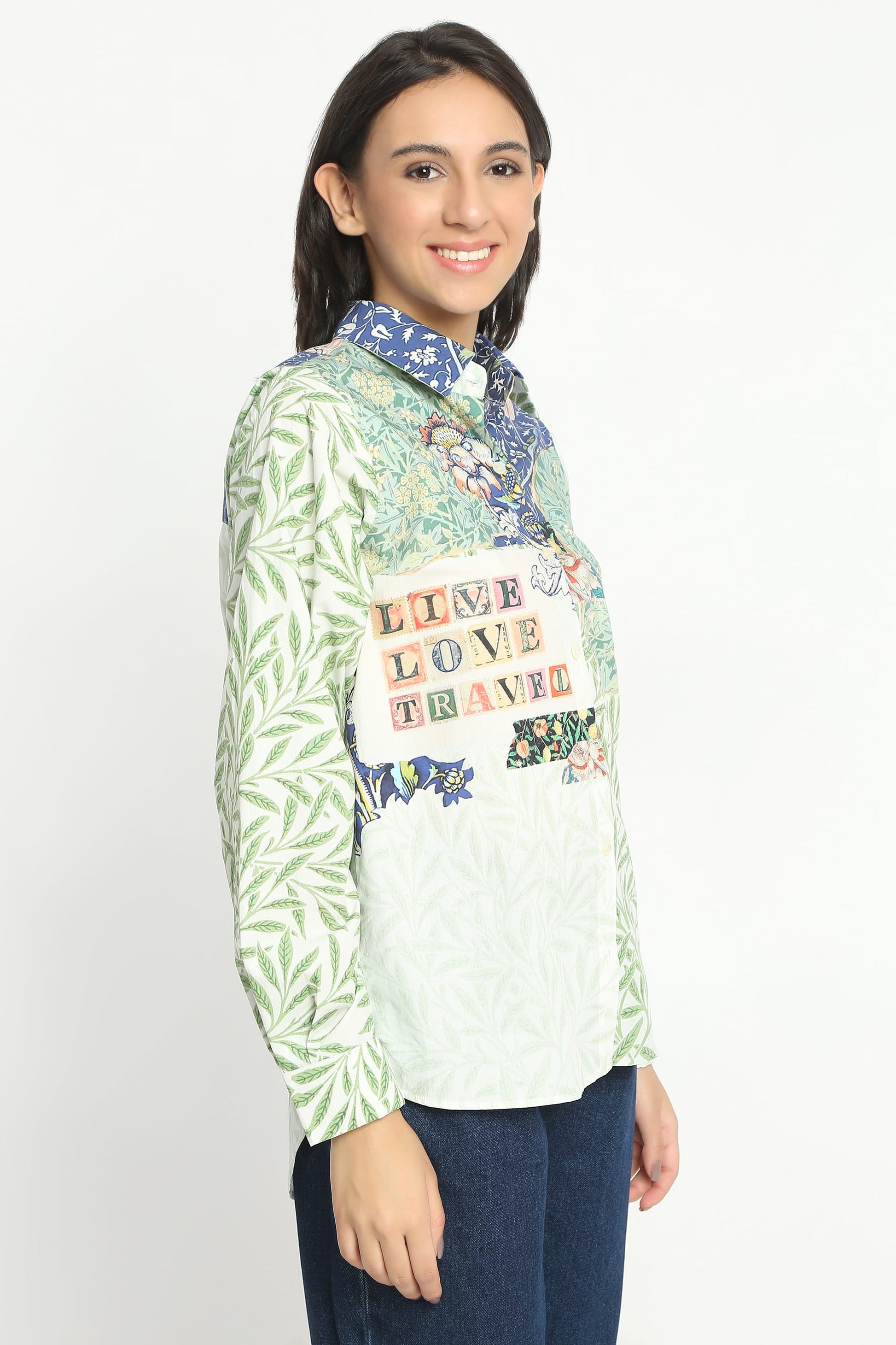 A woman modeling a long-sleeve button-up shirt with a light green palm leaf pattern on the sleeves and a multicolor graphic print on the front featuring the words 'LIVE LOVE TRAVEL' and tropical illustrations.