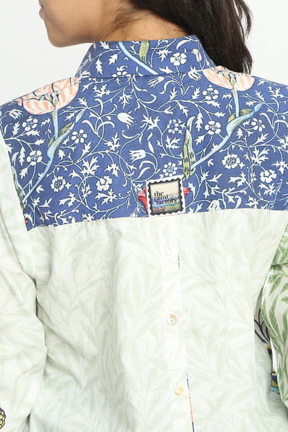 Close-up back view of a person wearing a collared button-up shirt with a blue floral yoke and an off-white textured body. A small square brand patch is visible near the collar.