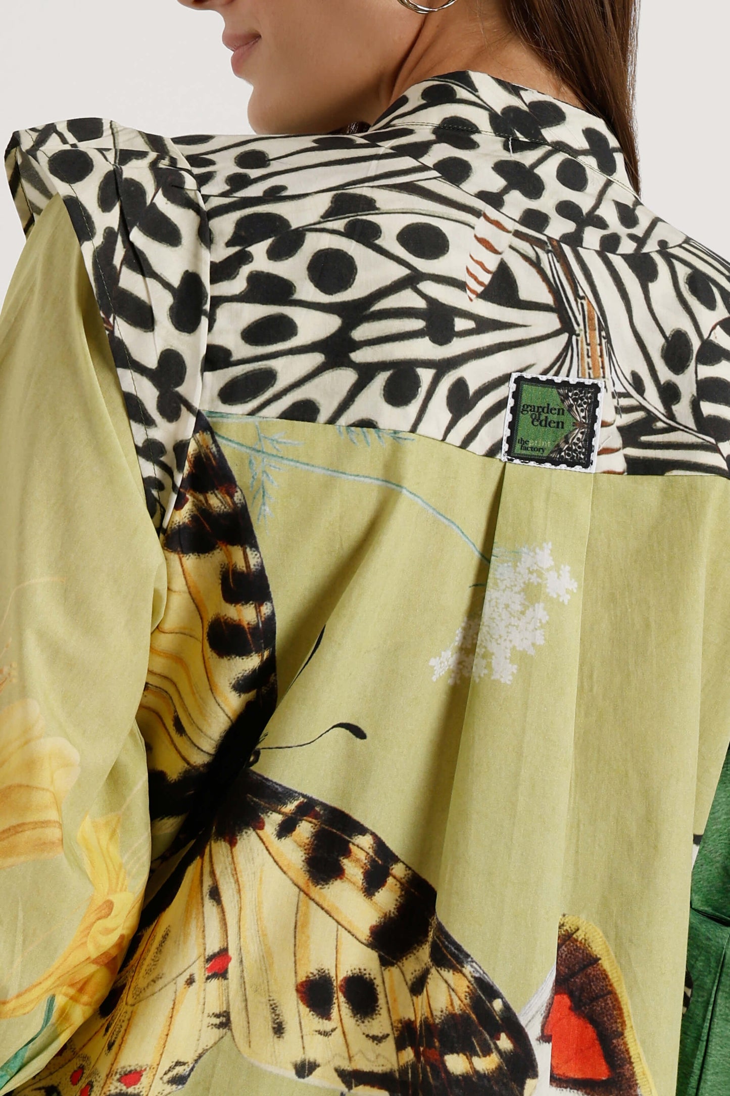 A close-up of a model wearing a patchwork silk blouse with a black and white spotted pattern, a large yellow butterfly print, and a green brand patch reading 'Gucci silk'.