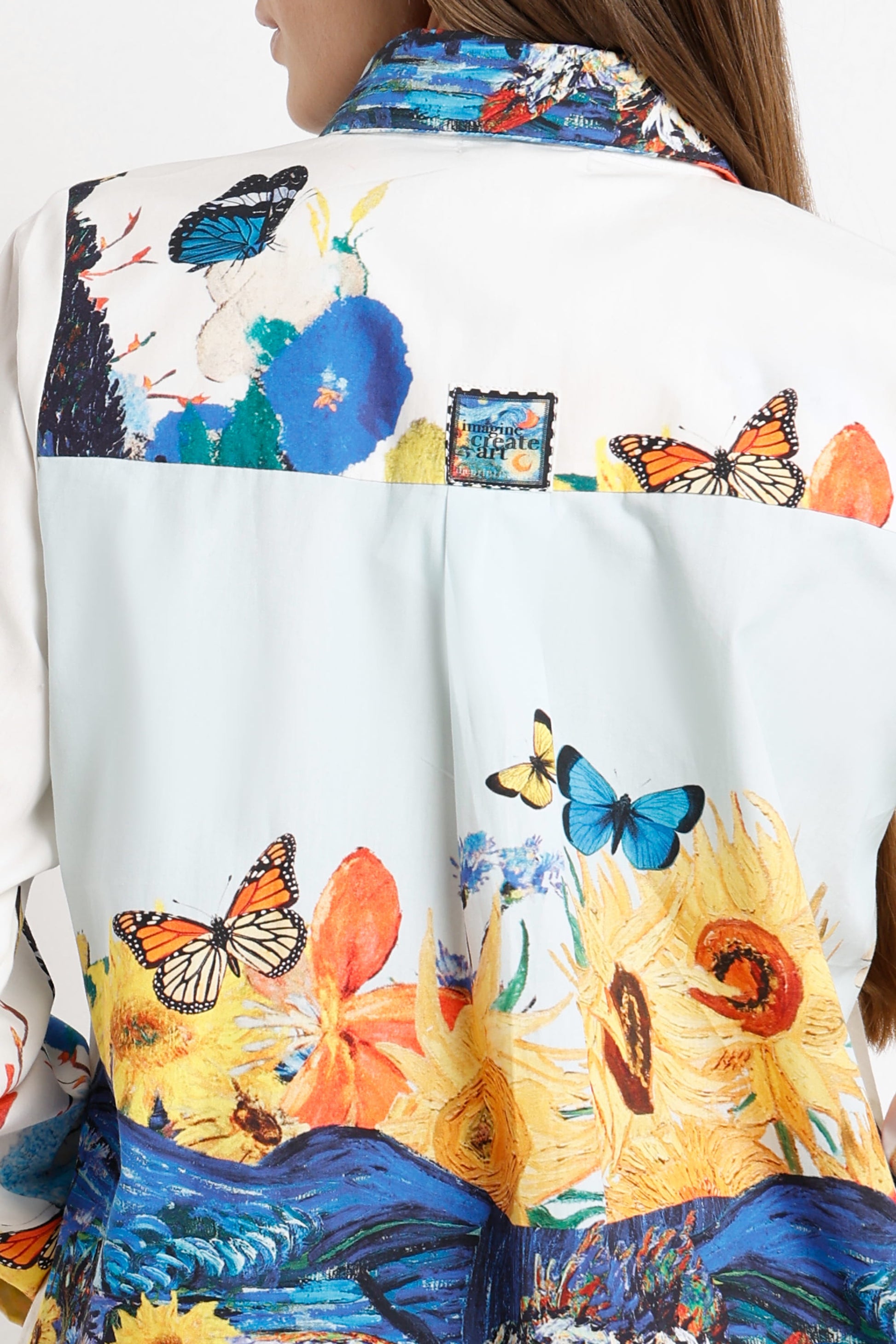Close-up of the back of a white shirt or jacket featuring a vibrant, multicolored artistic print with butterflies, flowers, and blue landscape motifs.