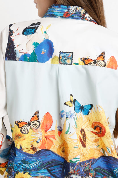 Close-up of the back of a white shirt or jacket featuring a vibrant, multicolored artistic print with butterflies, flowers, and blue landscape motifs.
