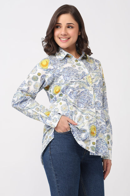 A woman modeling a long-sleeve button-up shirt with a blue and yellow floral print on a white background, paired with dark blue jeans, against a light gray studio background.