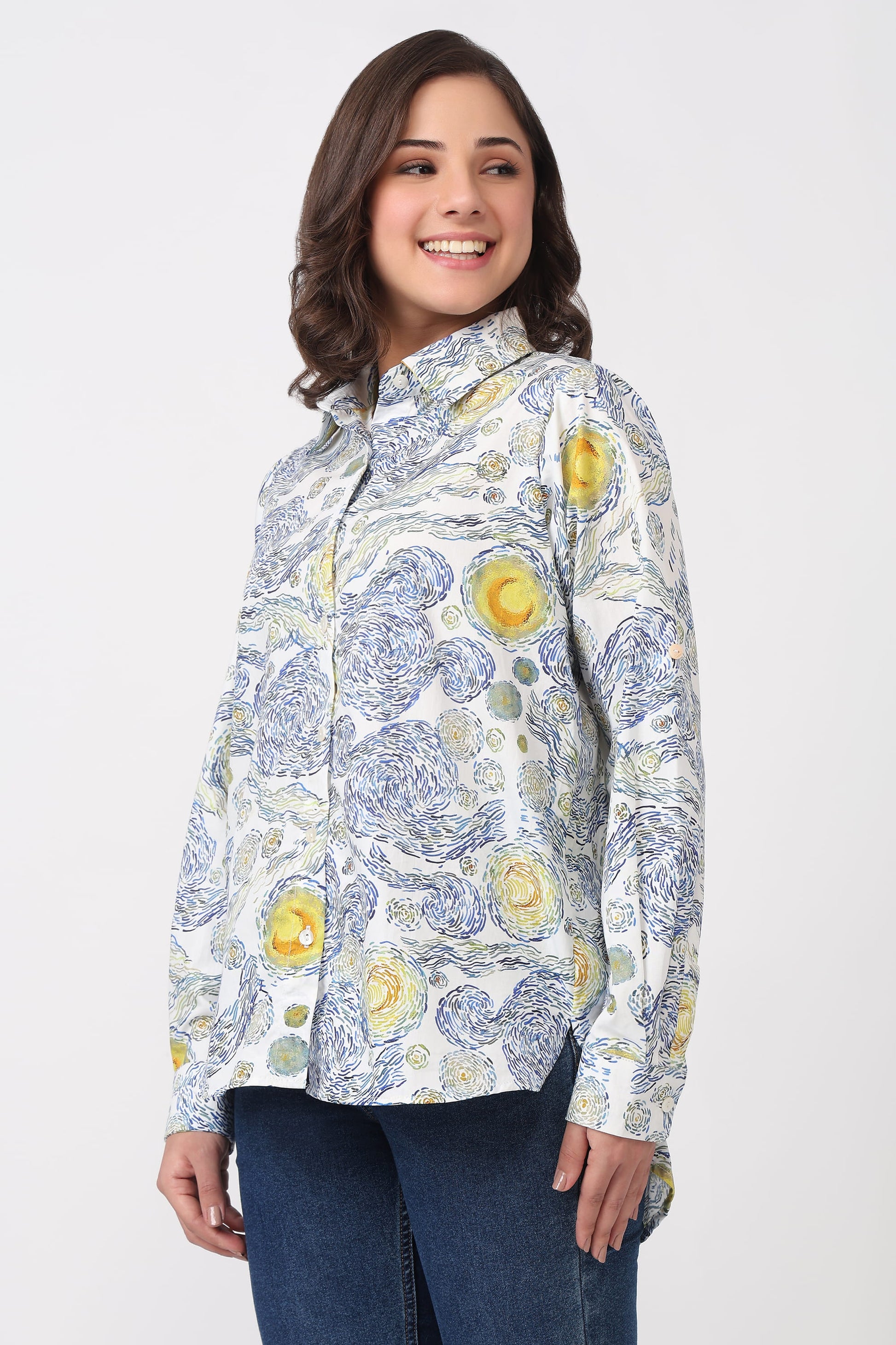 A woman modeling a long-sleeve button-up shirt with a blue and yellow floral pattern on a white background, paired with dark blue jeans, against a light gray studio backdrop.