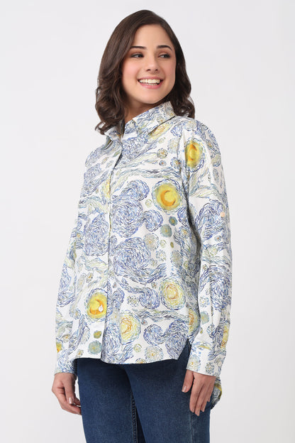 A woman modeling a long-sleeve button-up shirt with a blue and yellow floral pattern on a white background, paired with dark blue jeans, against a light gray studio backdrop.