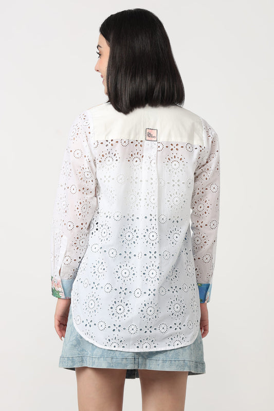 A woman shown from the back wearing a white long-sleeve eyelet lace blouse with a light blue denim skirt, against a plain light gray studio background.