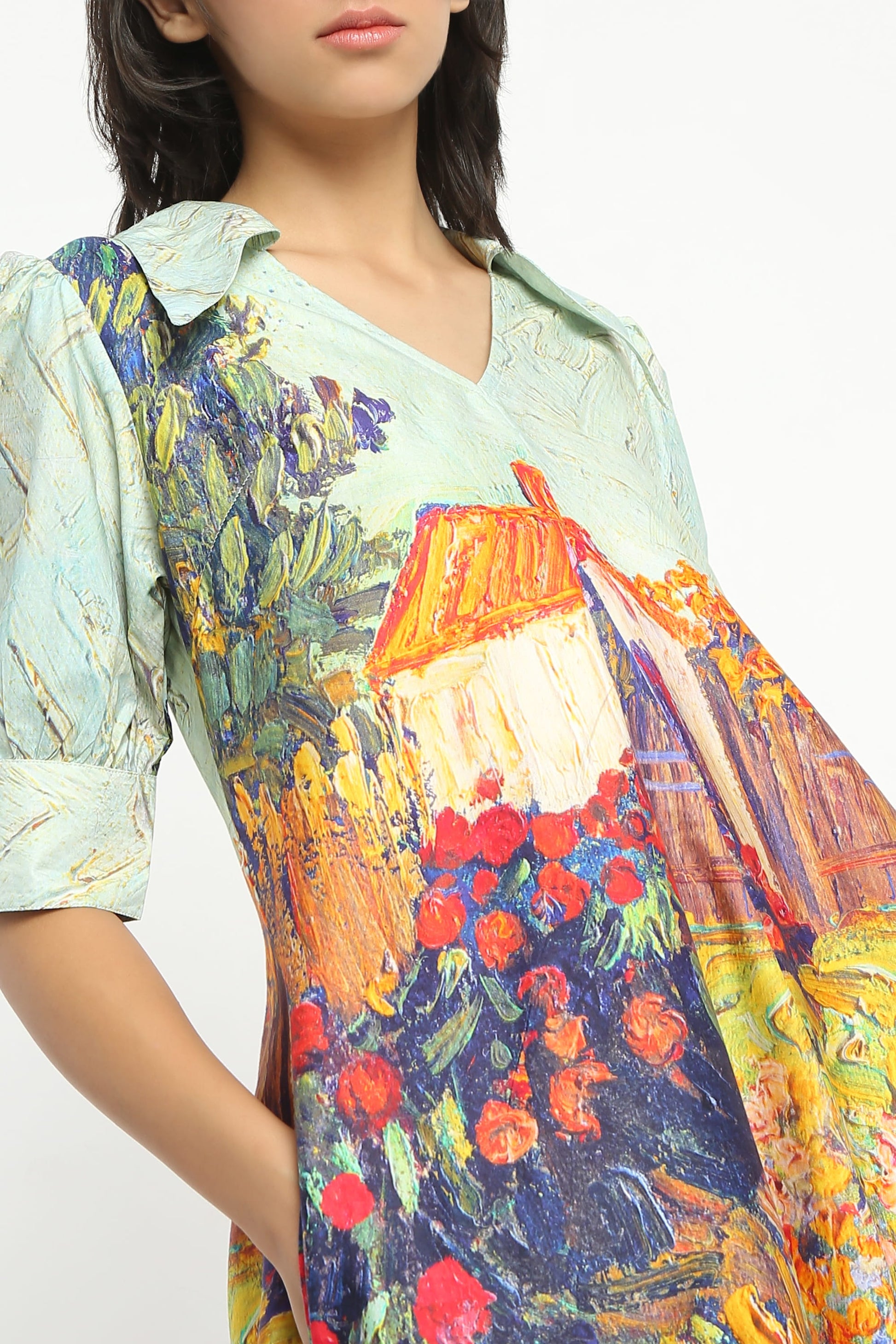 A woman wearing  a short puff-sleeve dress with a multicolour floral and landscape print, paired with beige strappy high-heeled sandals, against a plain white studio background.