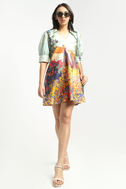 A woman wearing  a short puff-sleeve dress with a multicolour floral and landscape print, paired with beige strappy high-heeled sandals, against a plain white studio background.