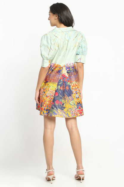 A woman wearing  a short puff-sleeve dress with a multicolour floral and landscape print, paired with beige strappy high-heeled sandals, against a plain white studio background.