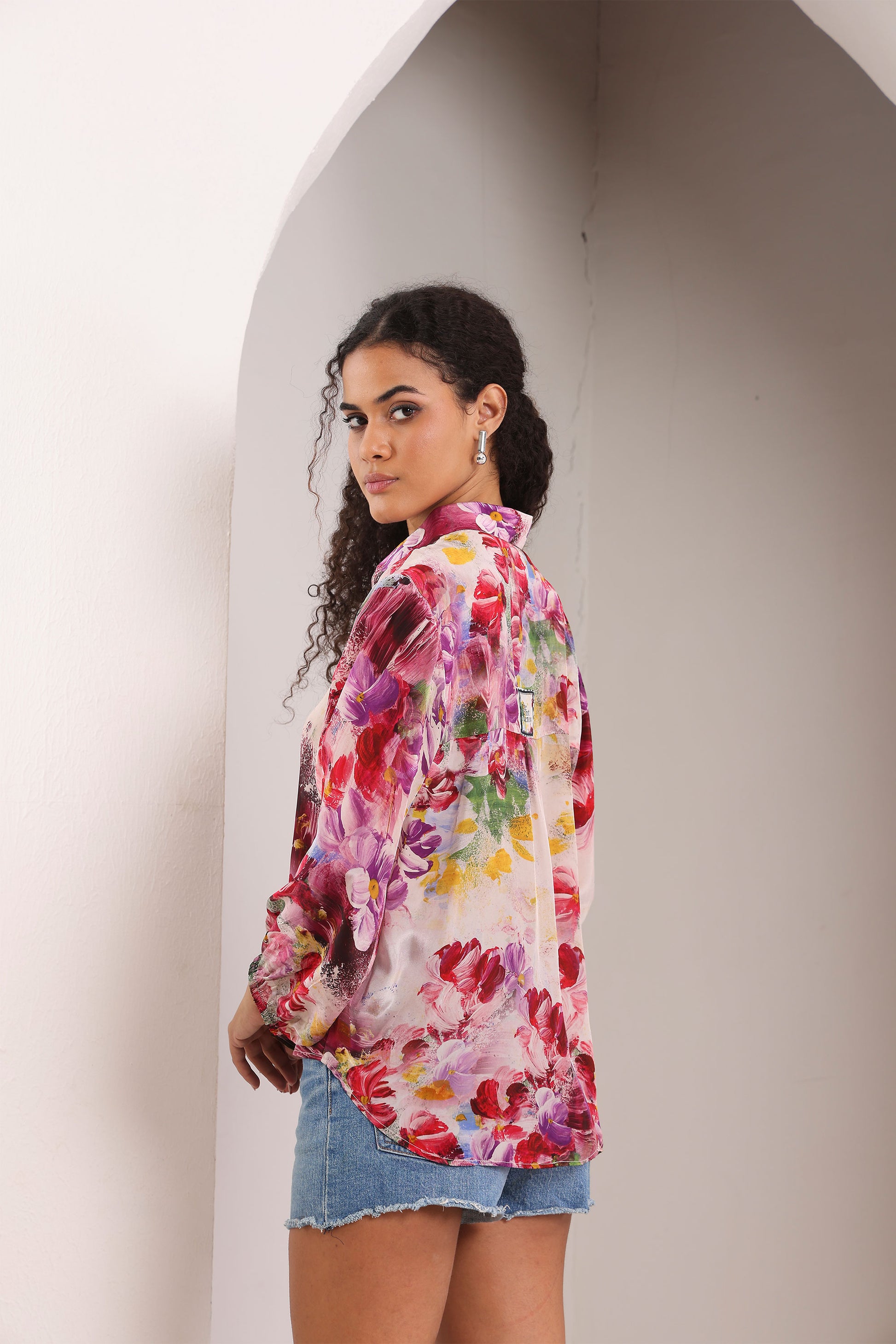 Woman wearing a colorful floral shirt standing against a plain wall.