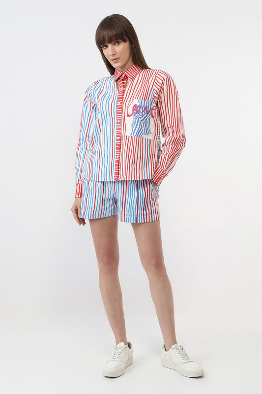 A model wearing a matching red, white, and blue striped shirt and shorts set with a colorful graphic pocket detail, paired with white sneakers, against a plain white studio background.