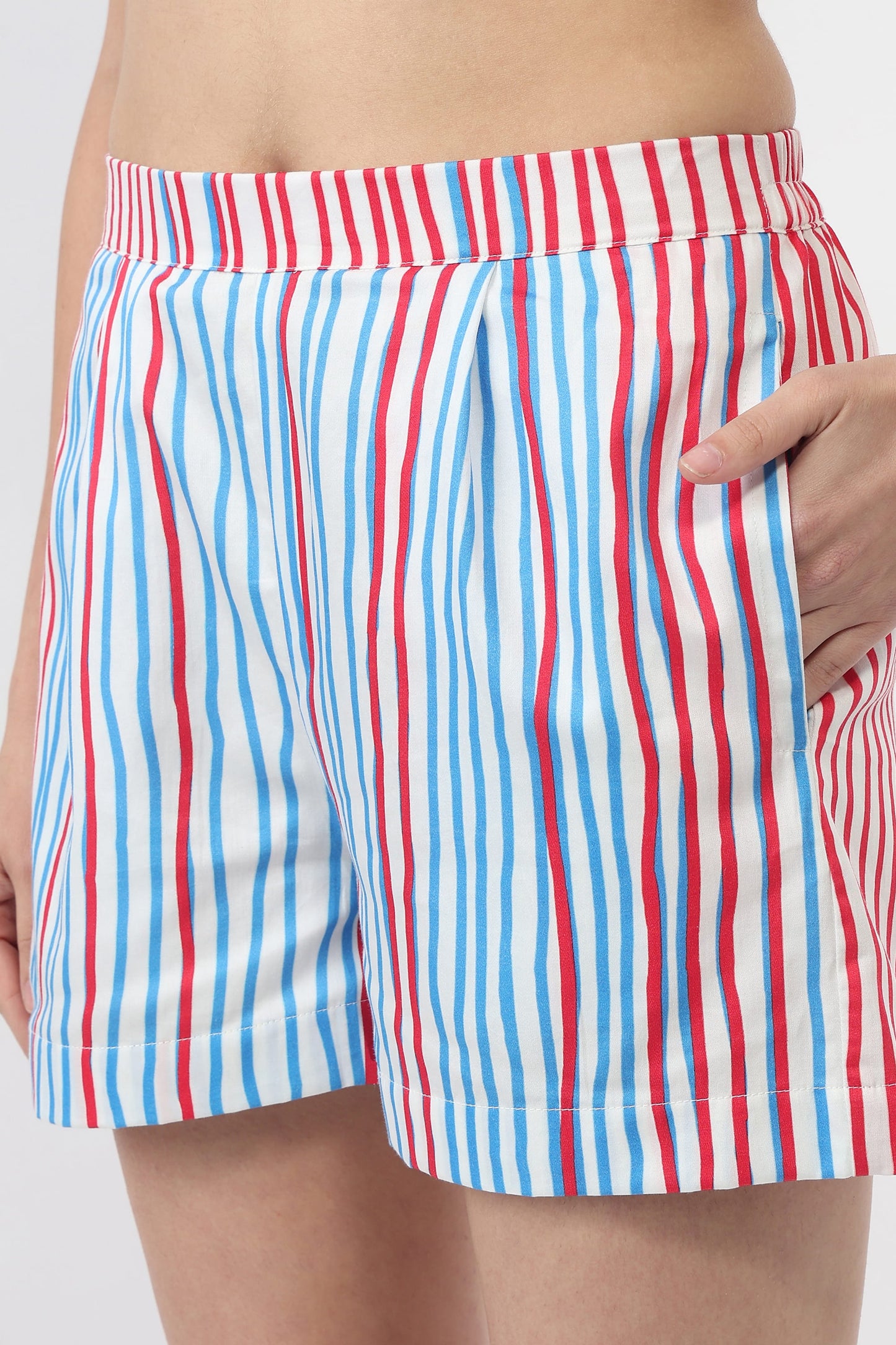 A close-up of a person wearing striped shorts with vertical red, white, and blue stripes, showing the side pocket and hand.