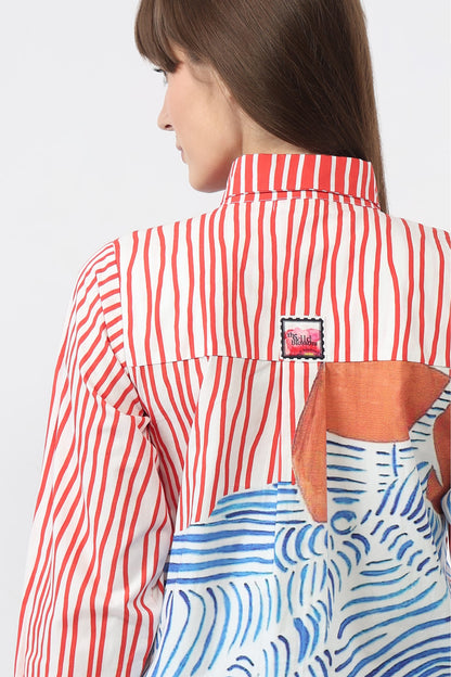 A woman shown from the back wearing a collared shirt with red and white vertical stripes on the upper back and a large abstract blue, white, and orange print patch on the lower back. A small rectangular brand patch is visible near the collar.
