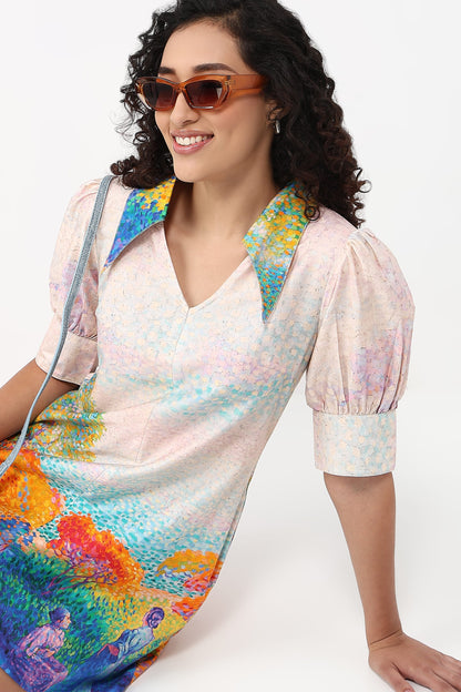 A woman wearing a short-sleeve V-neck dress with puff sleeves and a colorful painterly print, styled with brown sunglasses and a shoulder bag against a plain white background.