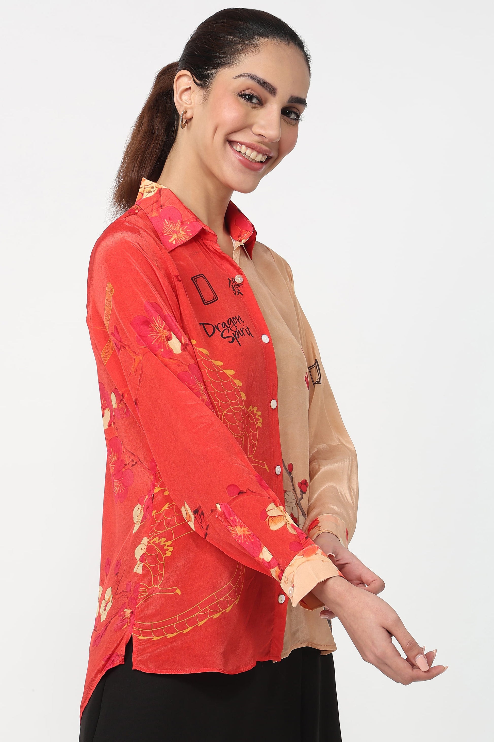 A woman wearing a split-design button-up shirt with a red floral print on one side and a beige satin side on the other, posed against a plain light gray background.