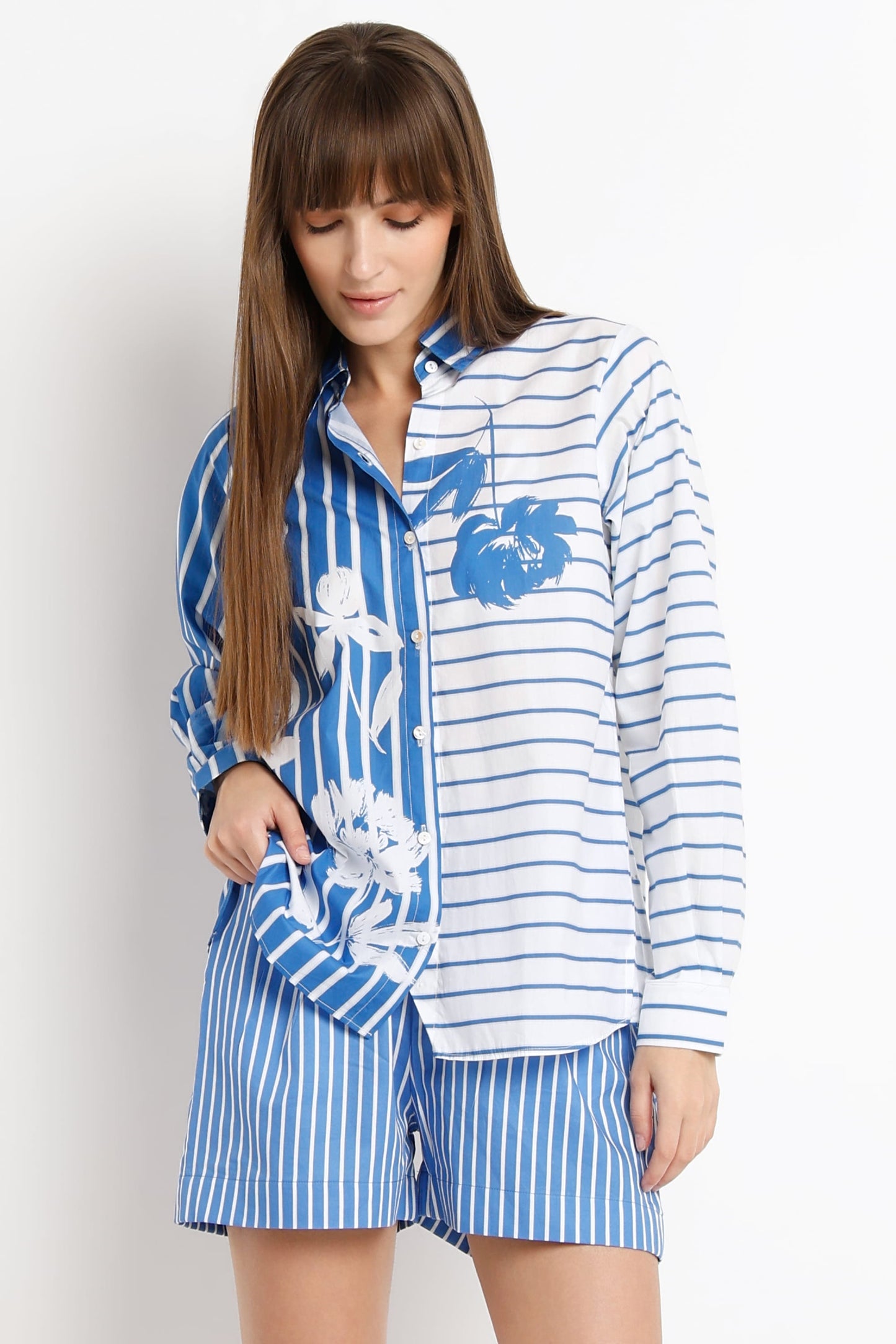 A woman modeling a matching two-piece pajama set with a blue and white striped shirt featuring a blue floral print on one side and white side panels, paired with matching blue and white striped shorts.