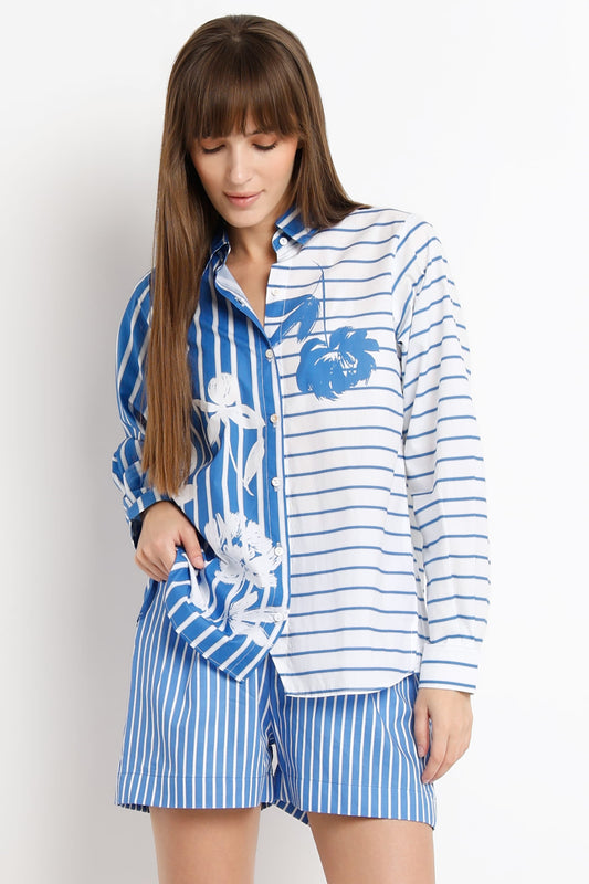 A woman modeling a matching two-piece pajama set with a blue and white striped shirt featuring a blue floral print on one side and white side panels, paired with matching blue and white striped shorts.