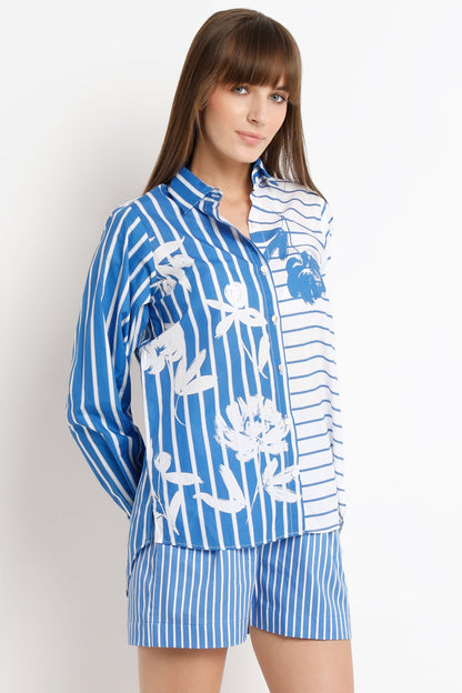 A woman modeling a matching blue and white striped pajama set with a floral print on the long-sleeve top and striped shorts, against a plain white studio background.