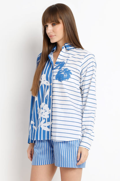 A woman modeling a matching two-piece lounge set featuring a long-sleeve button-up shirt and shorts. The shirt has a white base with blue horizontal stripes on one side and a blue floral print on the other, paired with matching blue and white vertically striped shorts.