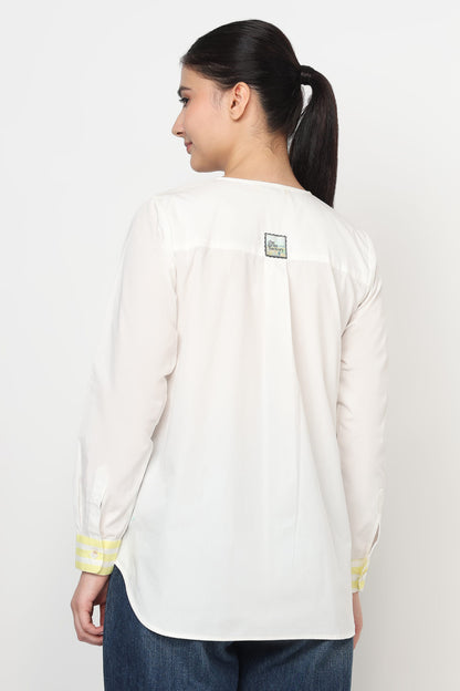 Woman wearing a white long-sleeve shirt with yellow accents on a plain background