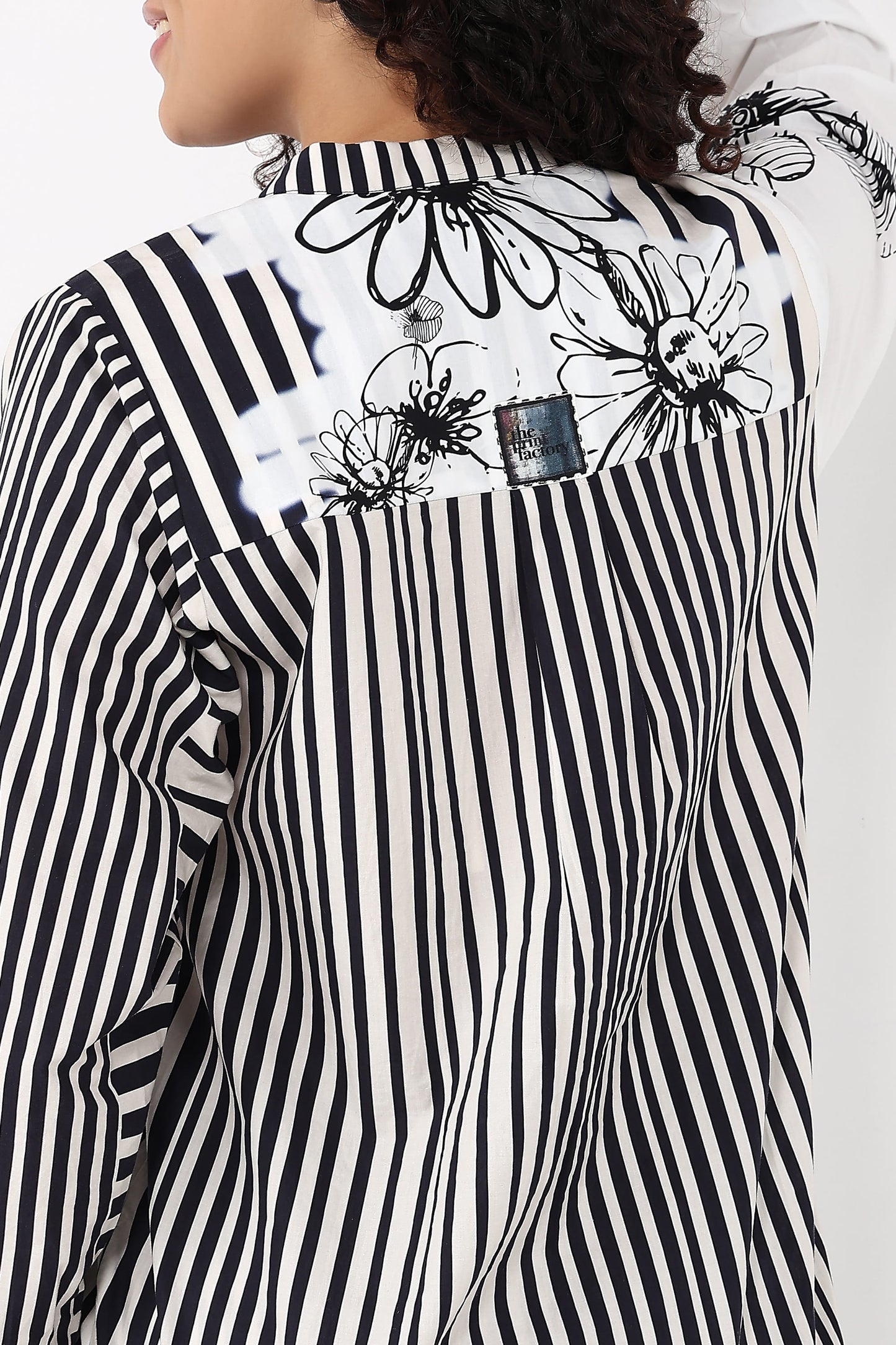 A close-up of a model wearing a black and white striped shirt with a floral print across the shoulders and a small denim patch detail.