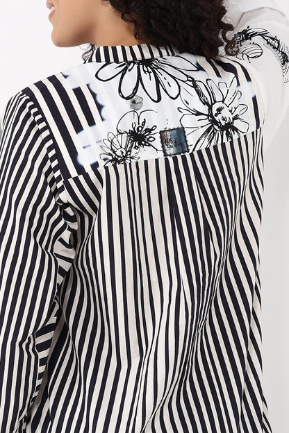 A close-up of a model wearing a black and white striped shirt with a floral print across the shoulders and a small denim patch detail.