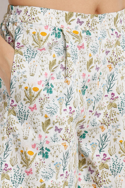 Close-up of a person wearing white drawstring shorts with a dense multicolor wildflower and butterfly print.